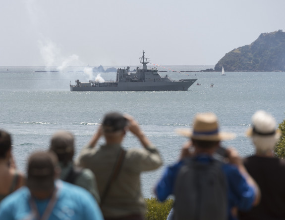 Smoke surrounds HMNZS Wellington as Ship's Company fire a 21 gun salute while a crowd observes at the Waitangi Treaty Grounds