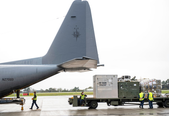Royal New Zealand Air Force personnel prepare the Hercules aircraft, loading on supplies. The image shows the back of the aircraft with things being loaded via the ramp.
