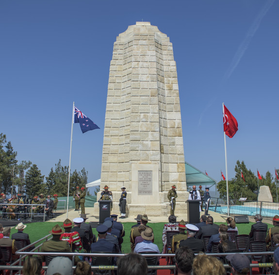 The New Zealand Memorial Service at Chunuk Bair, Gallipoli - in the centre of the image you can see the memorial with the NZ flag to the left and the Turkey flag on the right. It's a sunny day with blue sky.