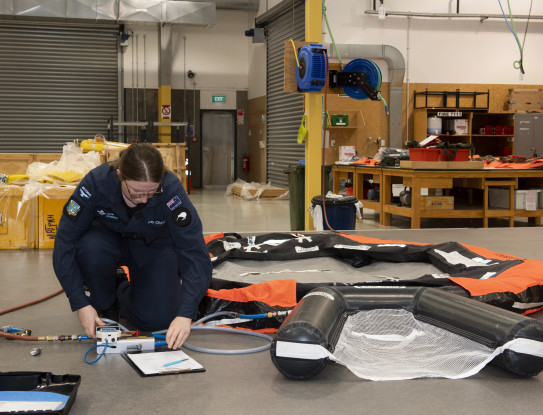 A Royal New Zealand Air Force Aviator working in the Liferaft Bay at Base Ohakea. There are liferafts and other equipment all over the floor. 