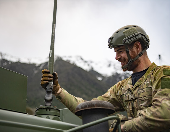 Personnel set up the antenna on the Pinzgauer in front of snow capped mountains.