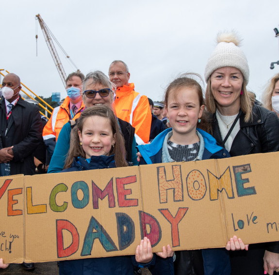 Family members wait to welcome HMNZS Te Mana at Devonport Naval Base - they are holding a sign that reads 'welcome home daddy'