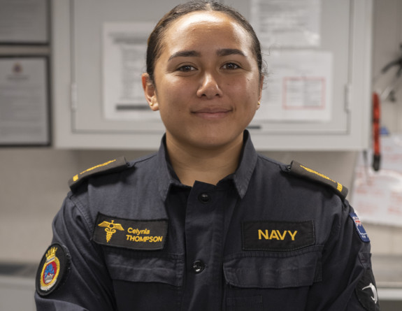 Abel Medic Celynia Thompson wearing a dark blue Navy uniform with gold accents stands facing the camera with her arms crossed.