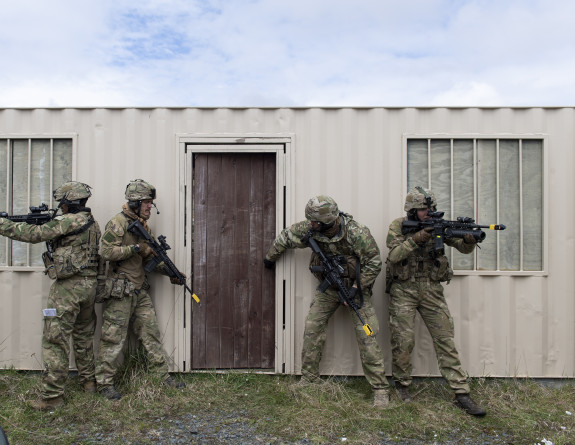 Four soldiers prepare to breach a container building, two soldiers are positioned each side of the door and the two soldiers on the outside keep watch,