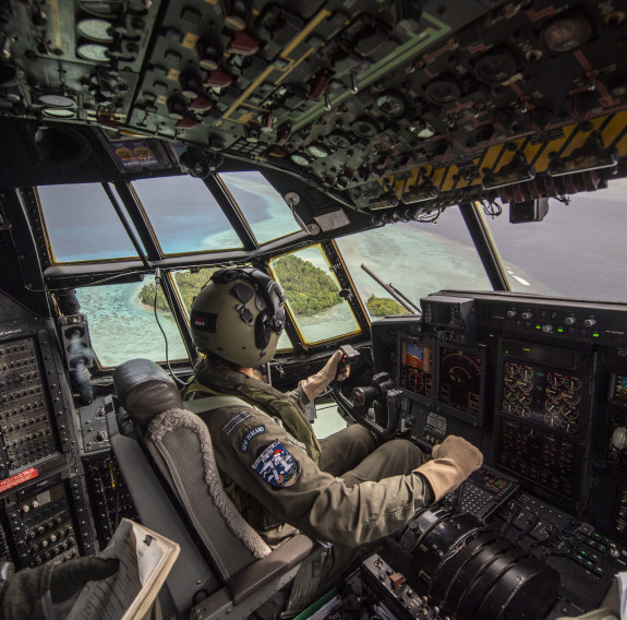 A pilot of the Hercules C-130 aircraft sits in the cockpit as they bank over a small tropical island.