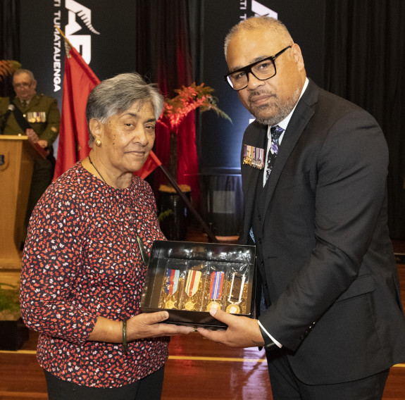 A woman receives a small case of medals from the Minister of Defence.