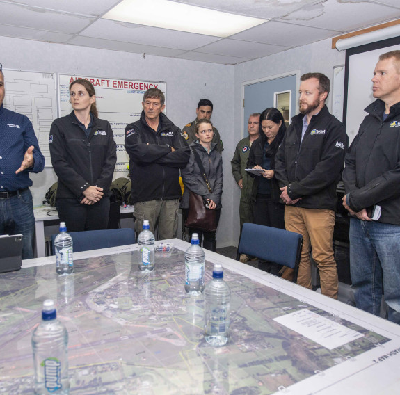 Prime Minister Chris Hipkins and Minister for Emergency Management Kieran McAnulty stand as they talk with other agencies around a large table at Base Auckland. 