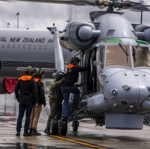 Prime Minister Chris Hipkins boards a Seasprite helicopter with No. 6 Squadron personnel at Base Auckland. In the background the Air Force Boeing 757 sits on the wet tarmac.