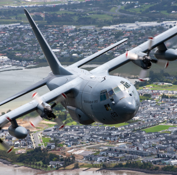 C-130H aircraft banks right as it flies over residential areas in Auckland. They grey p