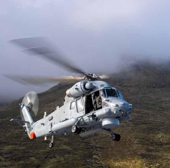 The sun light catches Seasprite helicopter as it hovers in front of the rugged terrain of Campbell Island.