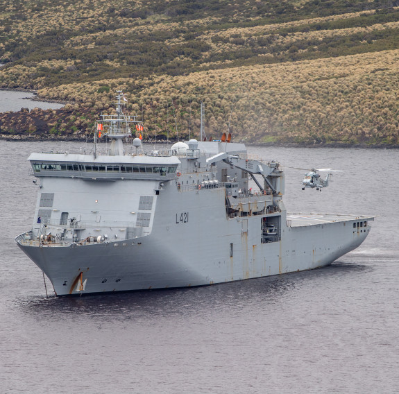 HMNZS Canterbury at anchor with a Seasprite helicopter taking off from the flight deck, Campbell Island during Op Endurance