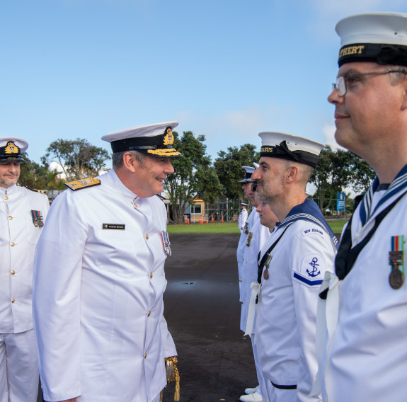 Deputy Chief of Navy inspects a rating's uniform on the parade ground of Devonport Naval Base under blue skies.