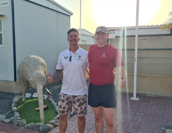CPL Norman (right) in baseball cap, t-shirt and shorts smiles at the camera with another person on base. They are both pulling a 'thumbs up' in front of a large sculpture of a kiwi.