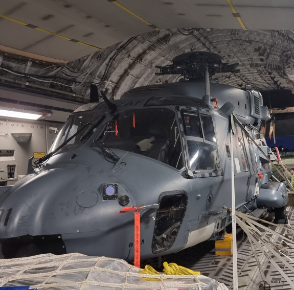 An NH-90 helicopter is loaded and strapped down in the RAAF C-17, lit by the interior lights of the aircraft. In the background, the rear door is still open.