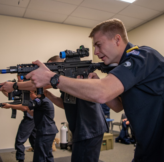 Four sailors and an instructor using the Mobile Weapons Simulator in an indoor environment at Devonport Naval Base