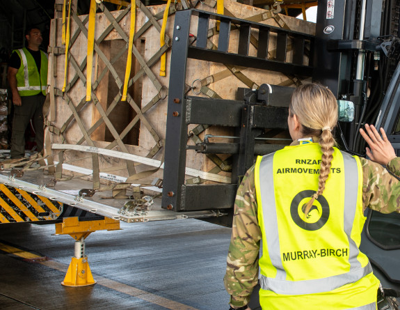 One of our Air Force personnel wearing camouflage uniform and a high vis vest guides goods into the rear of the C-130H(NZ) Hercules aircraft.