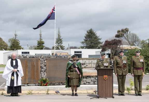Five Army personnel stand in front of the memorial wall during the opening ceremony. The New Zealand flag is flying near the wall.