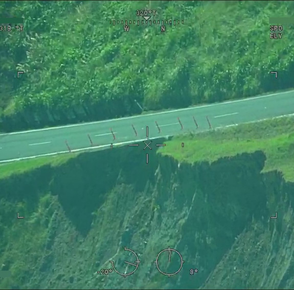 Aerial image of a landslide very close to a road with only a wooden stake fence between them. 