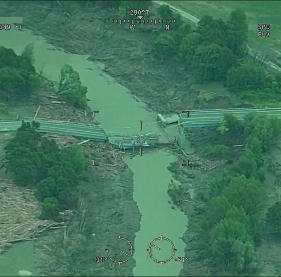Aerial image of a broken bridge over a river caused by Cyclone Gabrielle. Trees and debris is strewn either side of the river to the edges of the frame.