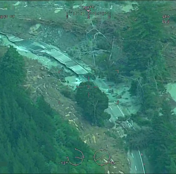 Aerial photo of a road that flows through a valley completely destroyed with only parts of the road visible. Lots of water and debris is present.