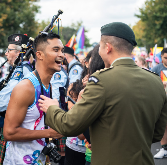 A soldier talks with a civilian member of the parade. The civilian is wearing athletic clothing and smiles brightly at the soldier.