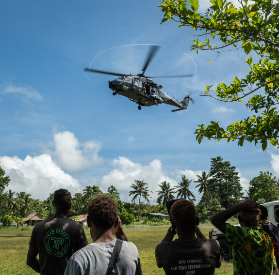 A helicopter comes in to land as people look on, on a sunny day. 