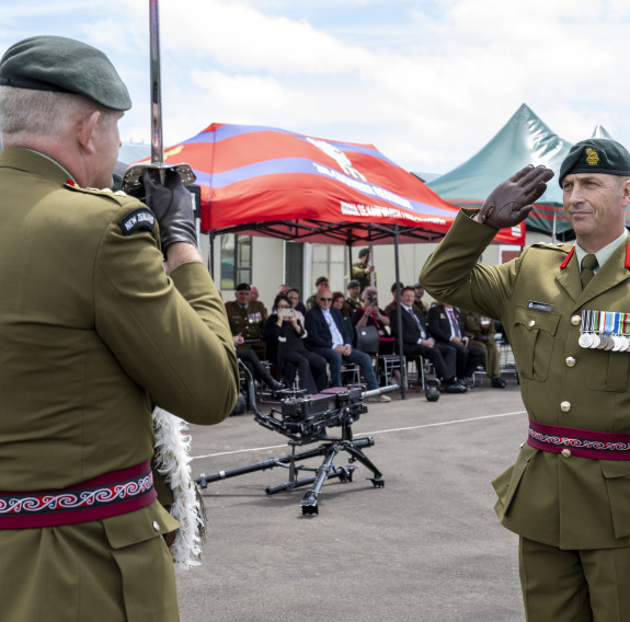 A soldier salutes with a sword to another soldier who returns the salute.