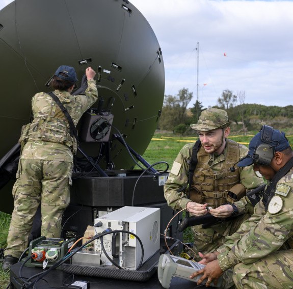 Three aviators set up a satellite dish in the field under the clouds.