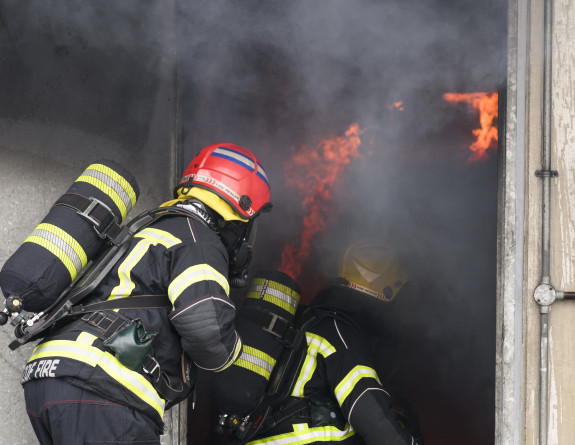 Personnel in firefighting gear fight fire at doorway, had their backs to the camera.