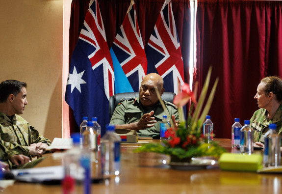 Uniformed military personnel sit around a boardroom table. There are three flags behind the person at the head of the table - the Australian, the Fijian and NZ flag. 