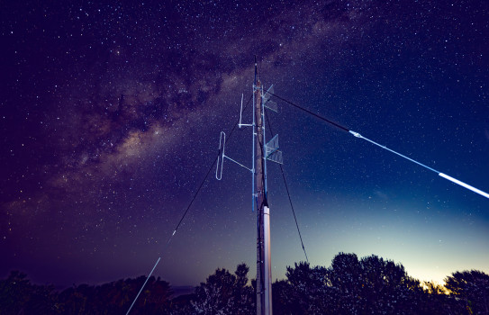 A low angle perspective of a communication tower that stands tall under the Milky Way and the night sky.