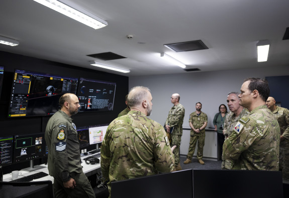 Uniformed personnel stand in a room talking. There are screens on the wall. 