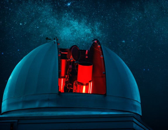 The Defence Science Technology telescope sits under the stars. The outer dome opens across the centre to reveal a glowing red telescope.