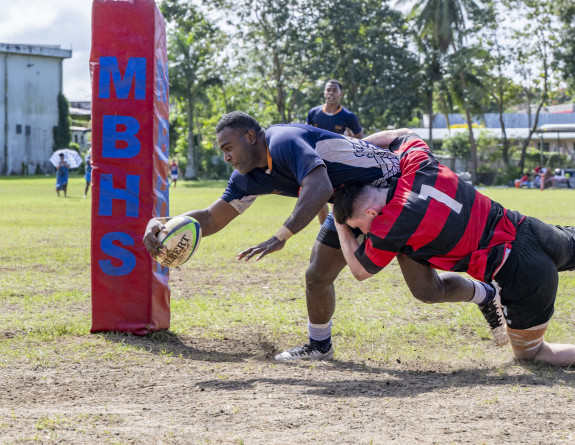 A rugby player gets a try as another player tackles him.