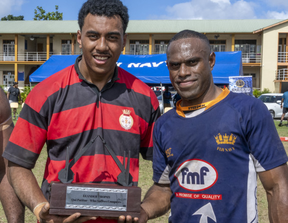 Two rugby players from different teams hold a trophy.