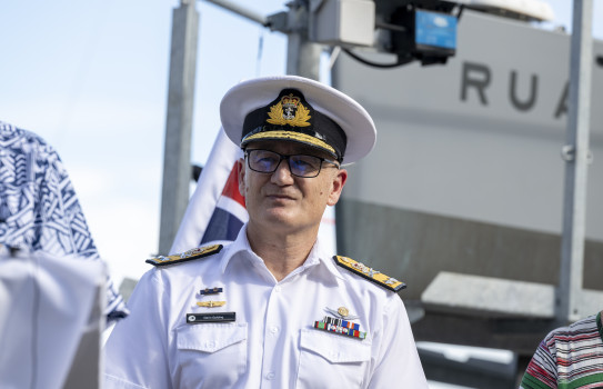 The Chief of Navy stands in front of the a flag and the Bluebottle USV on a trailer.