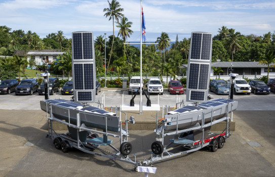 Two small vessels covered in solar panels sit on trailers in a car park in Fiji.