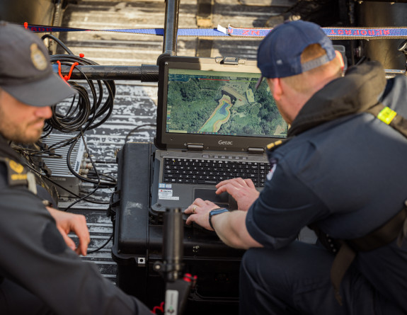 Two sailors look at the chats on a laptop while in the dinghy.