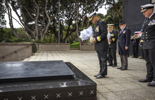 A man holding flowers in Navy uniform bows his head to the Tomb of the Unknown Warrior.