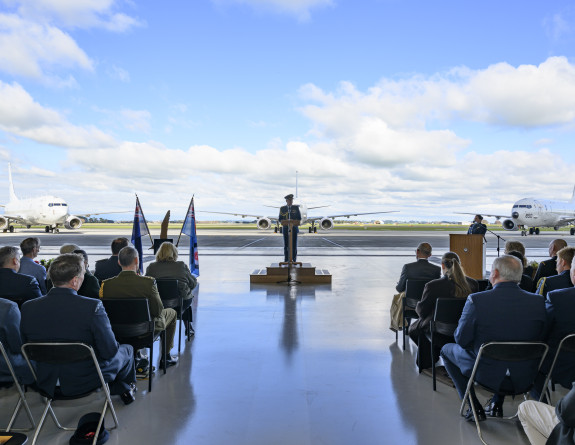 The Chief of Air Force speaks at a podium in the hander with three Poseidon aircraft on the tarmac behind him.