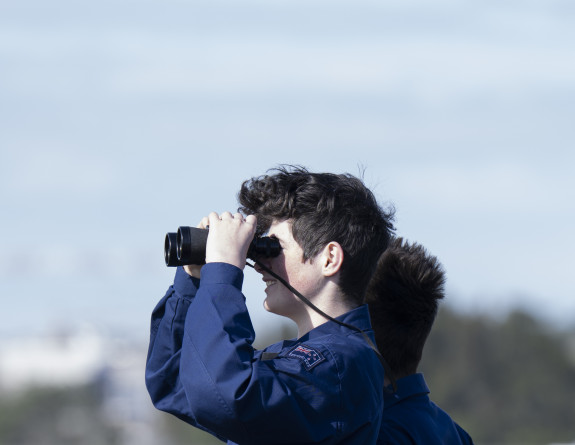 A cadet looks through binoculars on the tarmac.