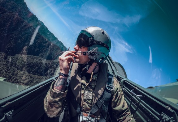 A pilot sits in the cockpit, looking out the window on a sunny day. 