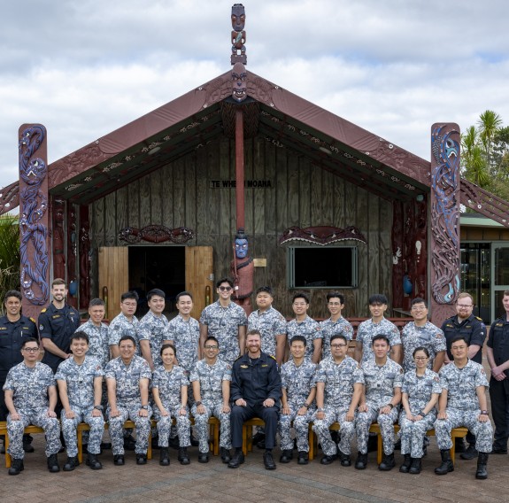 A group photo of personnel sitting positioned in front of a marae.