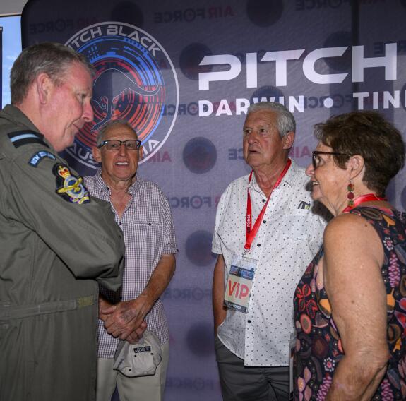 Three people talk with an aviator in front of Pitch Black branded wall.