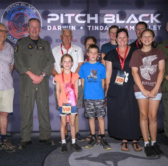 Standing in front of a Pitch Black banner, the family pose for a photo with two aviators. Lots of smiles at the camera.