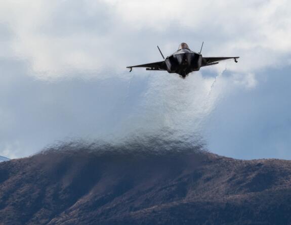 An RAAF F-35A approaching the Waiouru Training Area in the background there is a hill range and on far left you can see snowcapped mountains. You can see a heat haze out the bottom of the jet