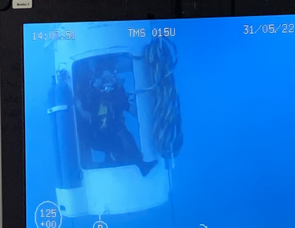 A diver is lowered to the seafloor in a diving bell to conduct an inspection.
