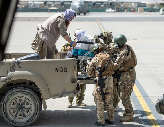 Four New Zealand Defence Force personnel help get an evacuee in a wheelchair get off a truck