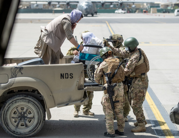 Four New Zealand Defence Force personnel help get an evacuee in a wheelchair get off a truck