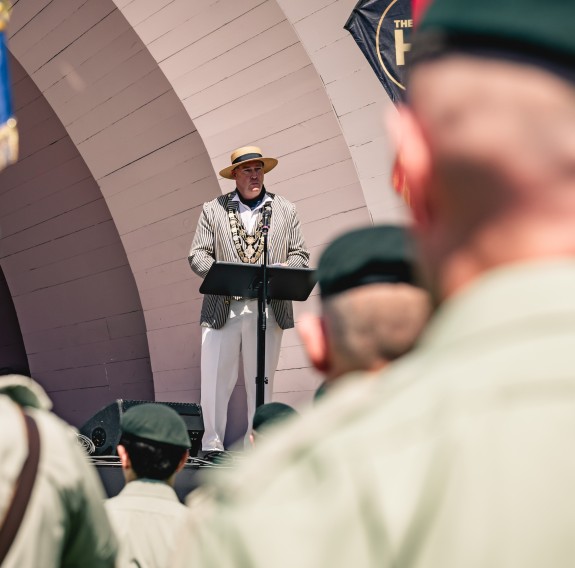 The rear of army personnel can be seen as they look on to the art deco stage.  The Mayor speaks to the crowd from a black lecturn.